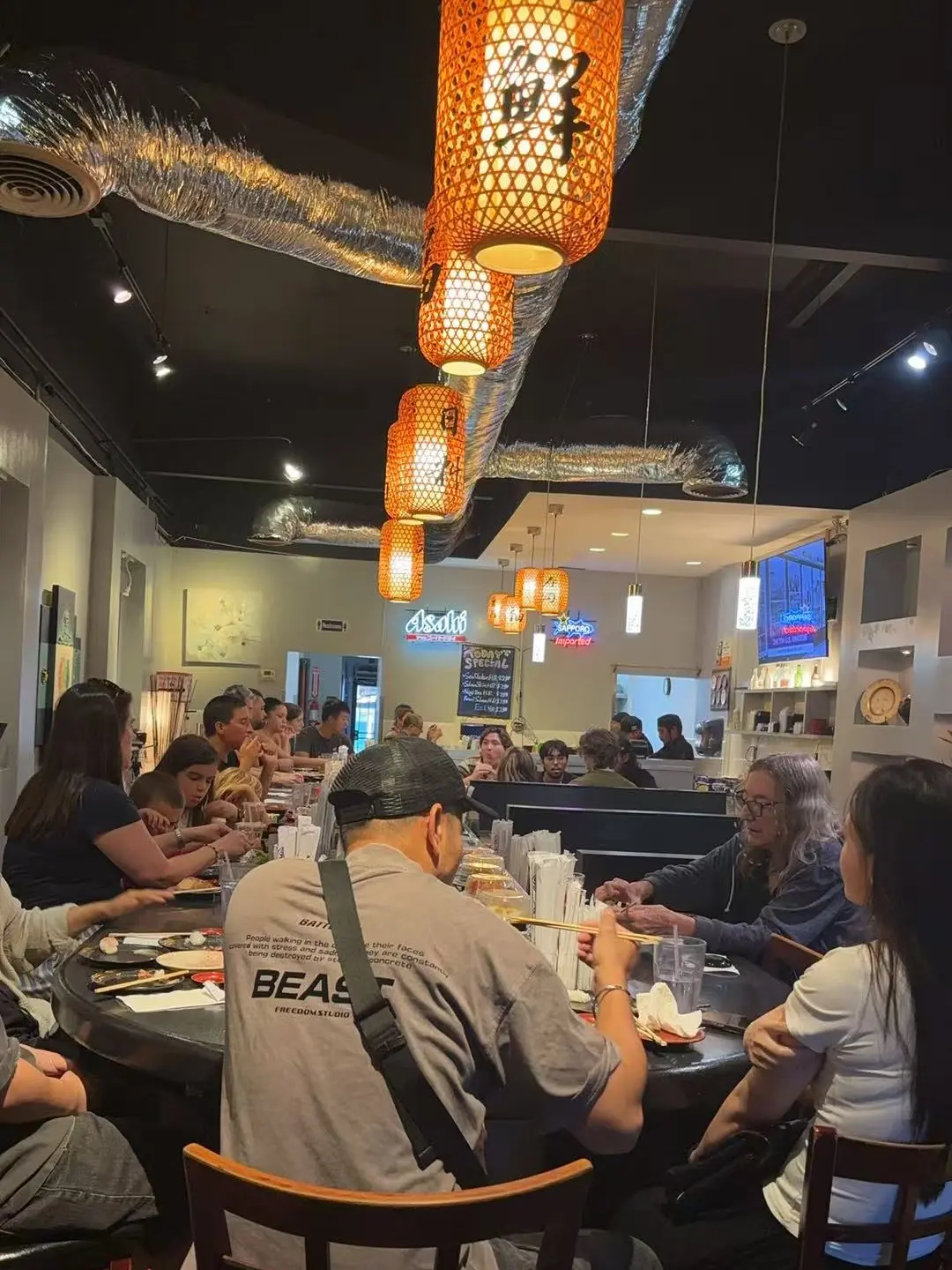 A full house around the oval belt counter at Kaisen Kaiten Sushi Bar, under Kaisen paper lanterns